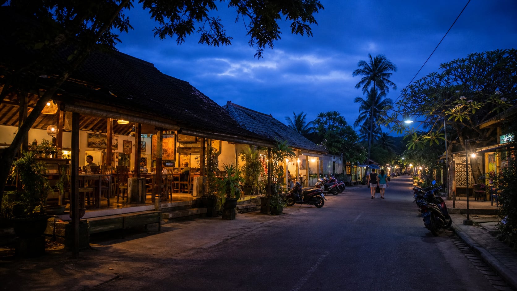 Dorfstraße in Pemuteran an Balis Nordwestküste am Abend mit Warungs und Rollern