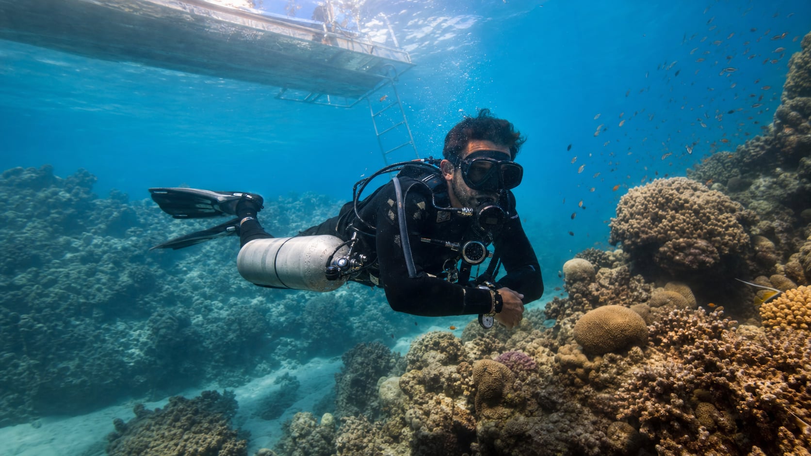 Taucher mit Sidemount-Konfiguration und seitlich angebrachten Tauchflaschen erkundet Korallenriff bei Koh Tao